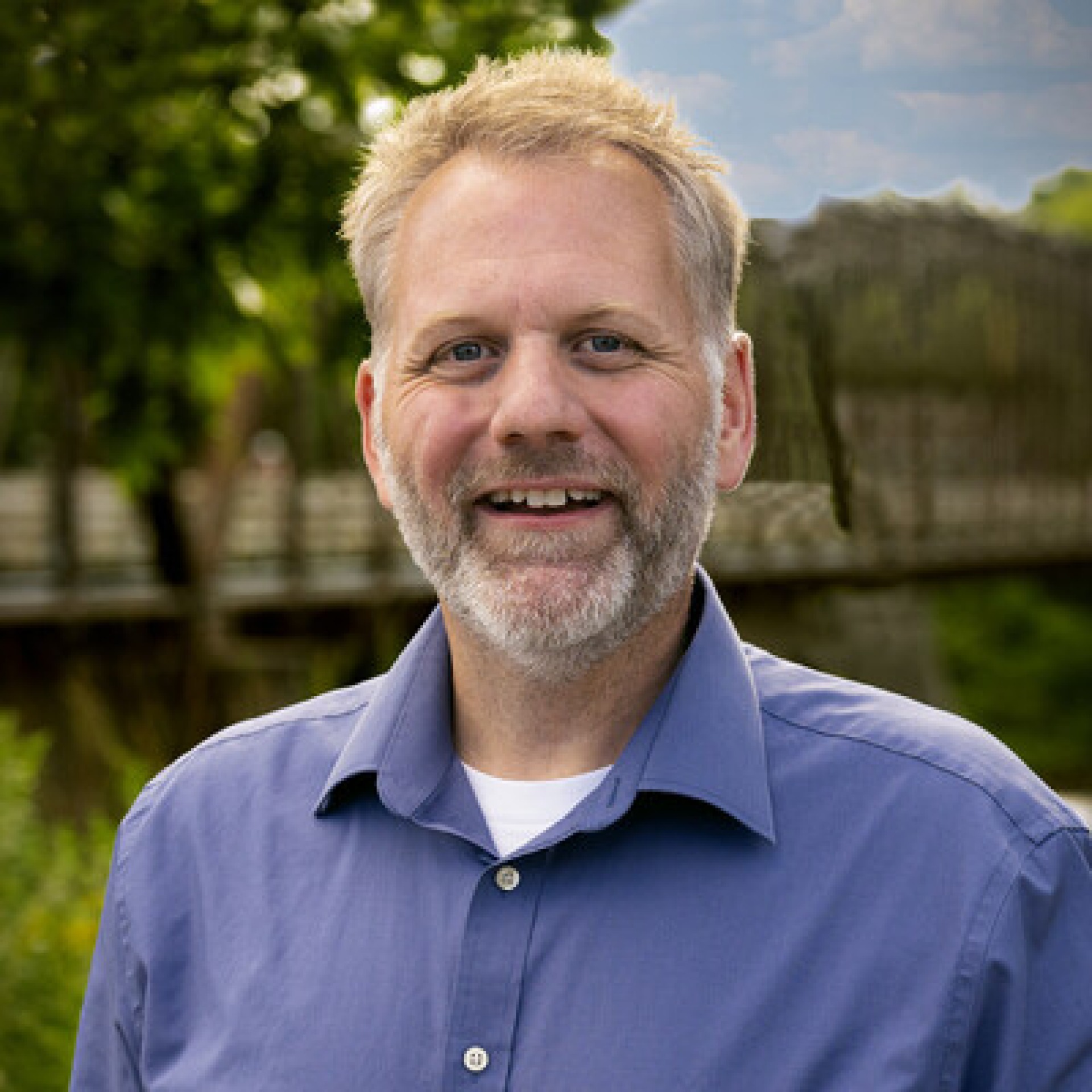 A white man wearing a blue flannel shirt smiles at the camera.