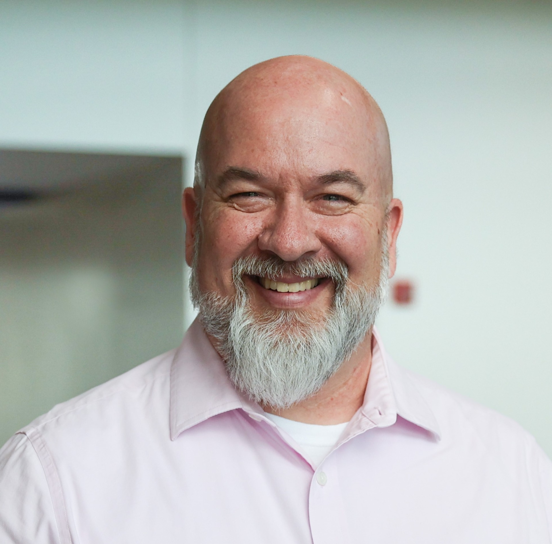 A headshot of a white man wearing a pink dress shirt.