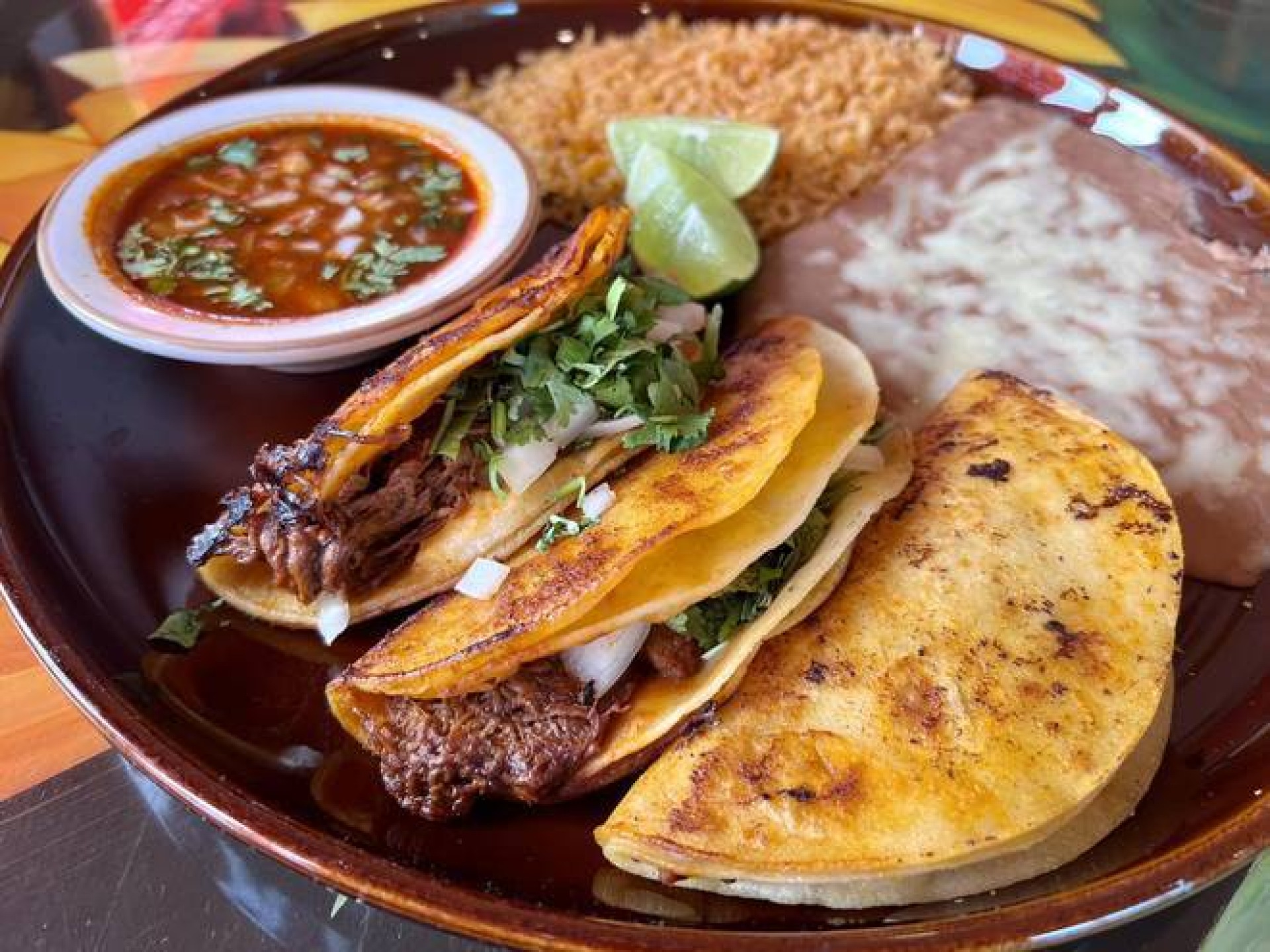 A Los Girasoles taco plate with three tacos, salsa, rice, and refried beans.